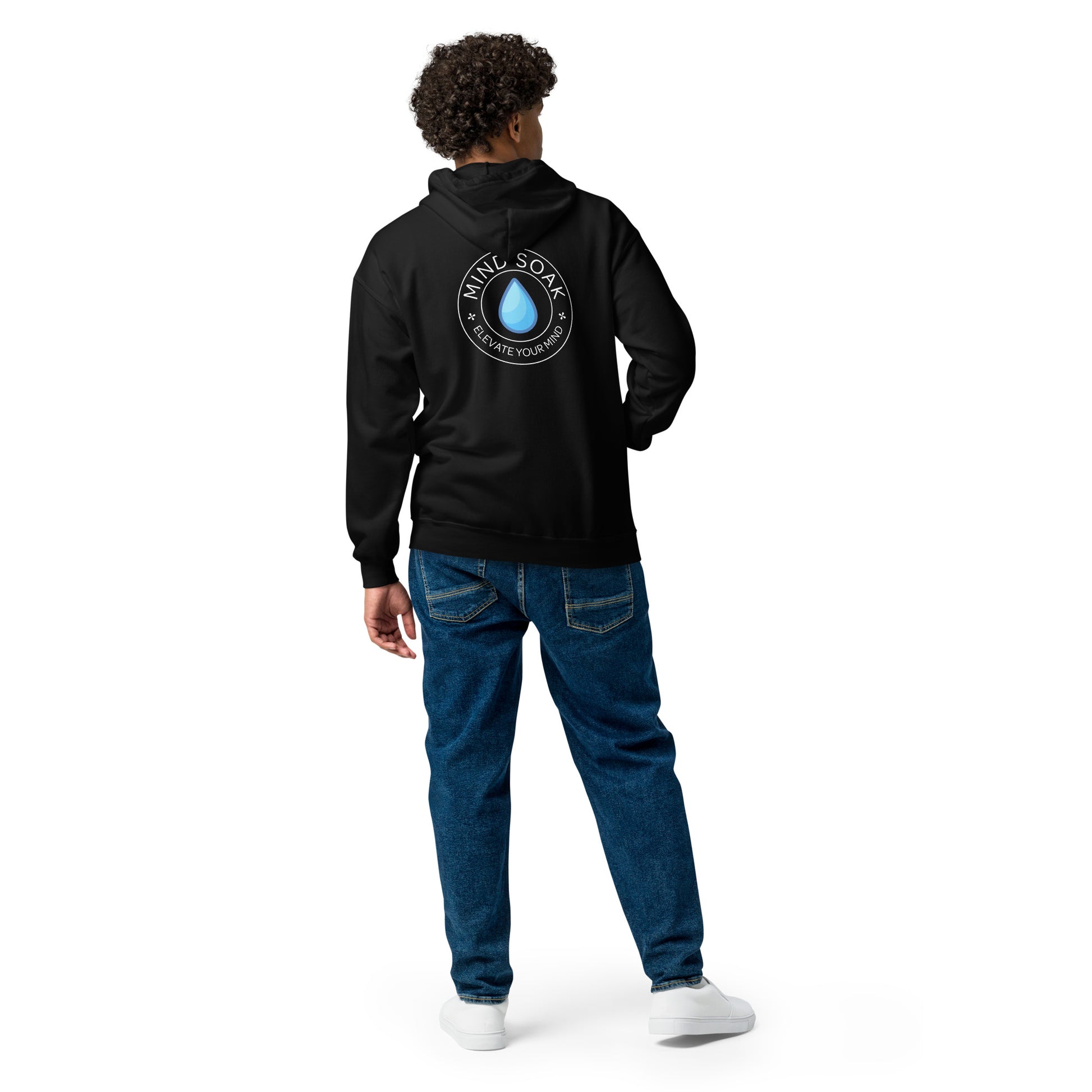 A man stands facing away, wearing a black Mind Soak graphic hoodie, medium-wash blue jeans, and white sneakers against a white background.