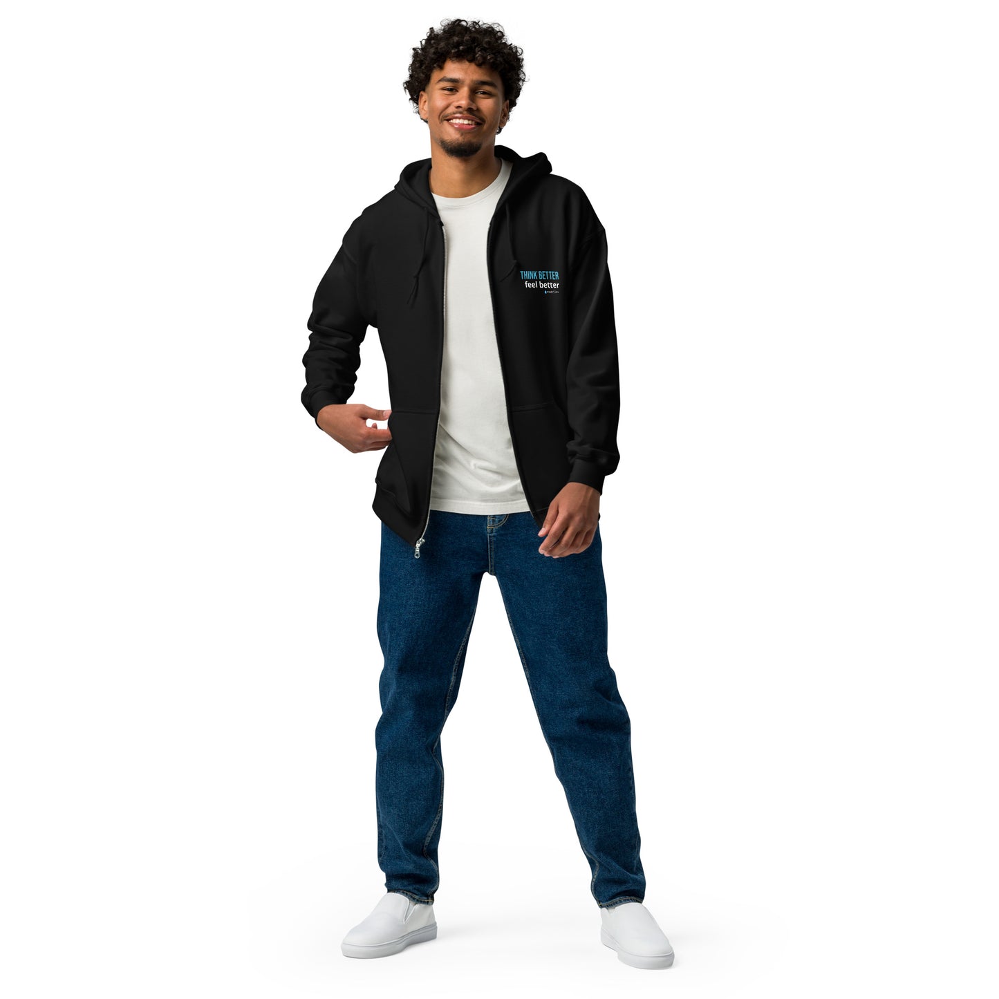 A man smiling in a black zip-up hoodie, white t-shirt, relaxed blue jeans, and white sneakers against a white background.